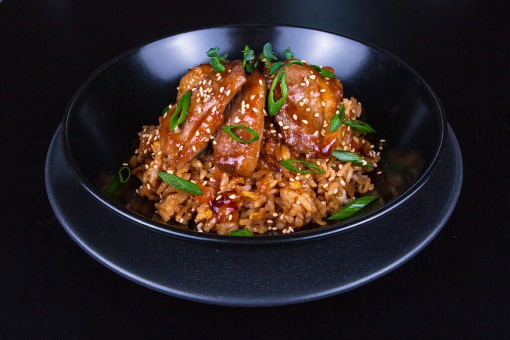 Kip teriyaki met sesamzaad en lente-ui op rijst in een zwarte kom