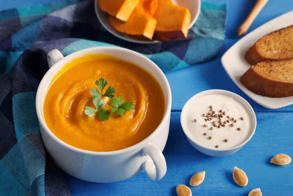 Romige pompoensoep met zoete aardappel in een kom, afgemaakt met pompoenpitten