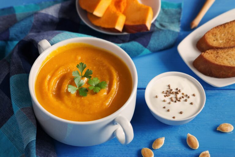 Romige pompoensoep met zoete aardappel in een kom, afgemaakt met pompoenpitten