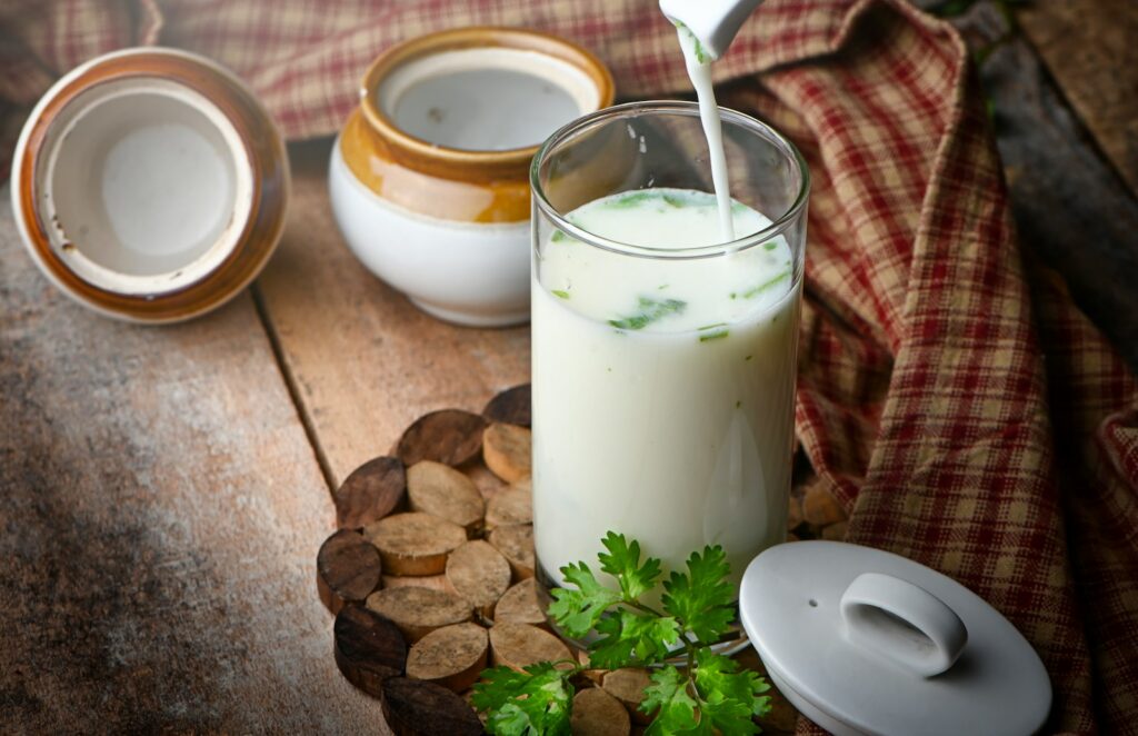 Glas melk naast groene bladeren als voorbeeld van calciumrijke voeding